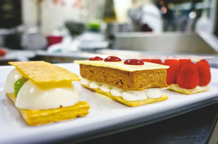 Three flaky layered pastries with raspberries, mousse and sabayon on a white countertop. 